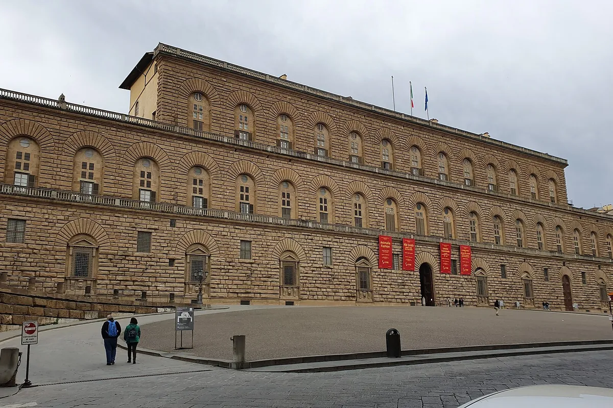 Dlouhá kamenná fasáda Palazzo Pitti ve Florencii, řady klenutých oken nad rustikálním zdivem