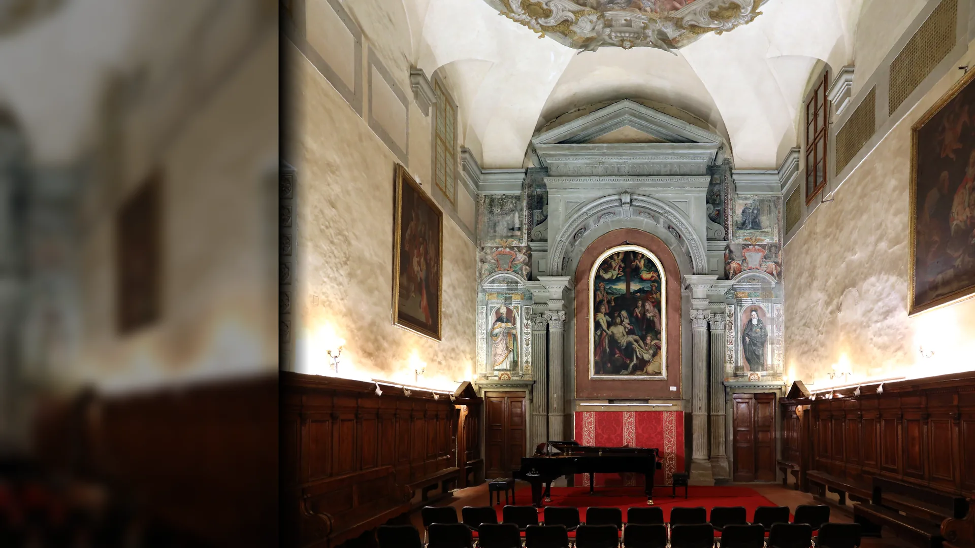 Skibet i Santa Monaca-kirken i Firenze er sat op til koncert: rækker af stole og et flygel på en rød løber foran et stensat alter med et malet altertavle, trækorstole langs begge vægge og et freskomaleri på hvælvingen ovenover